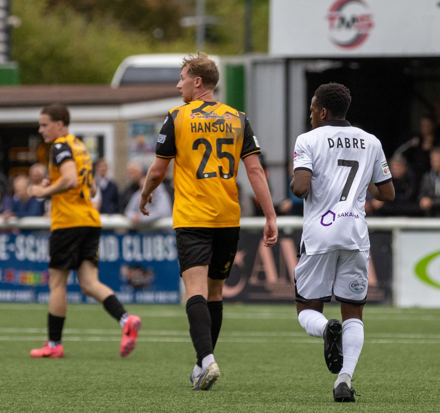Football players Hanson #25 and Dabre #7 walk on a green pitch during a competitive soccer match.