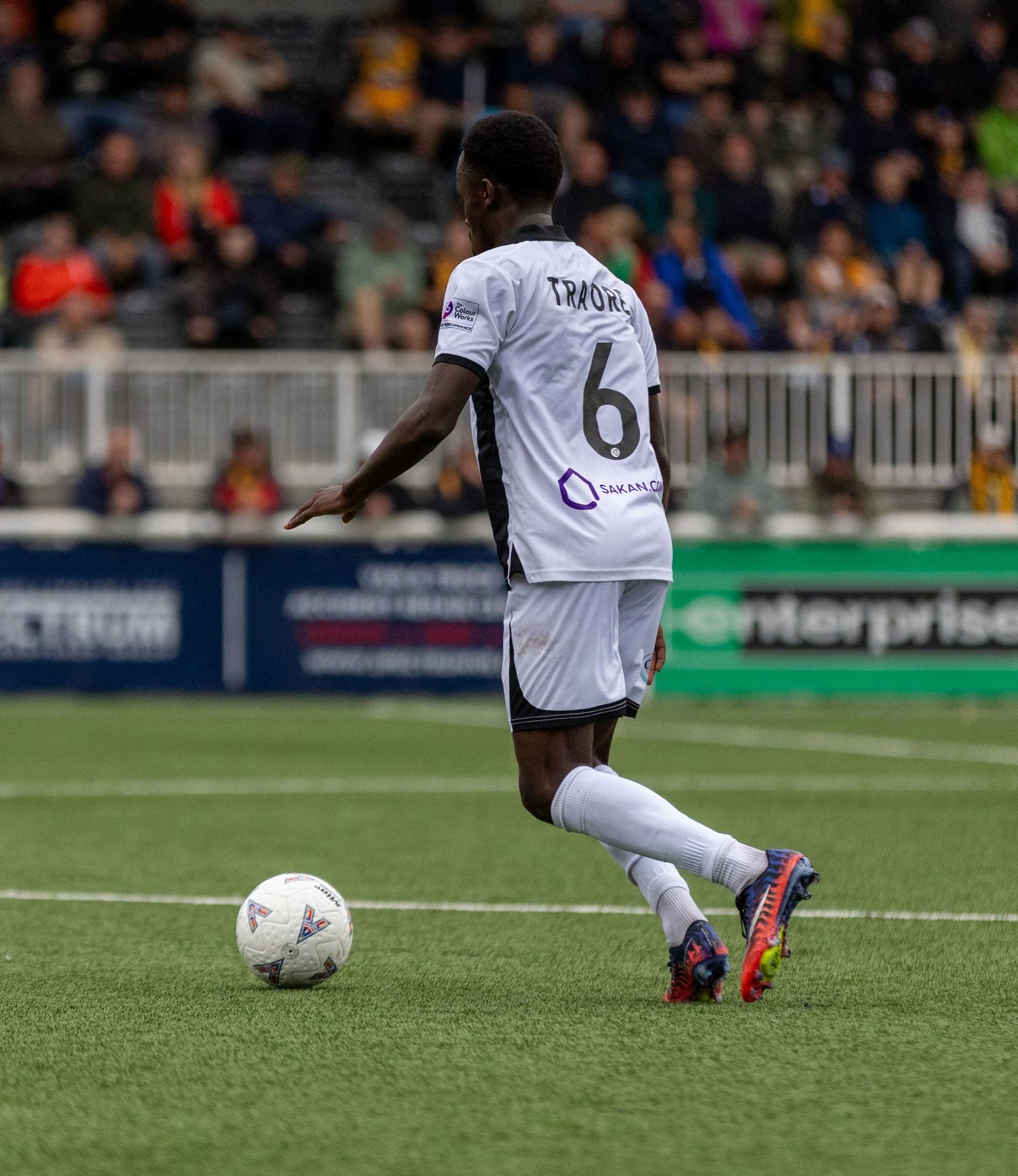 Football player wearing white number 6 jersey controls ball during competitive match on artificial turf pitch.
