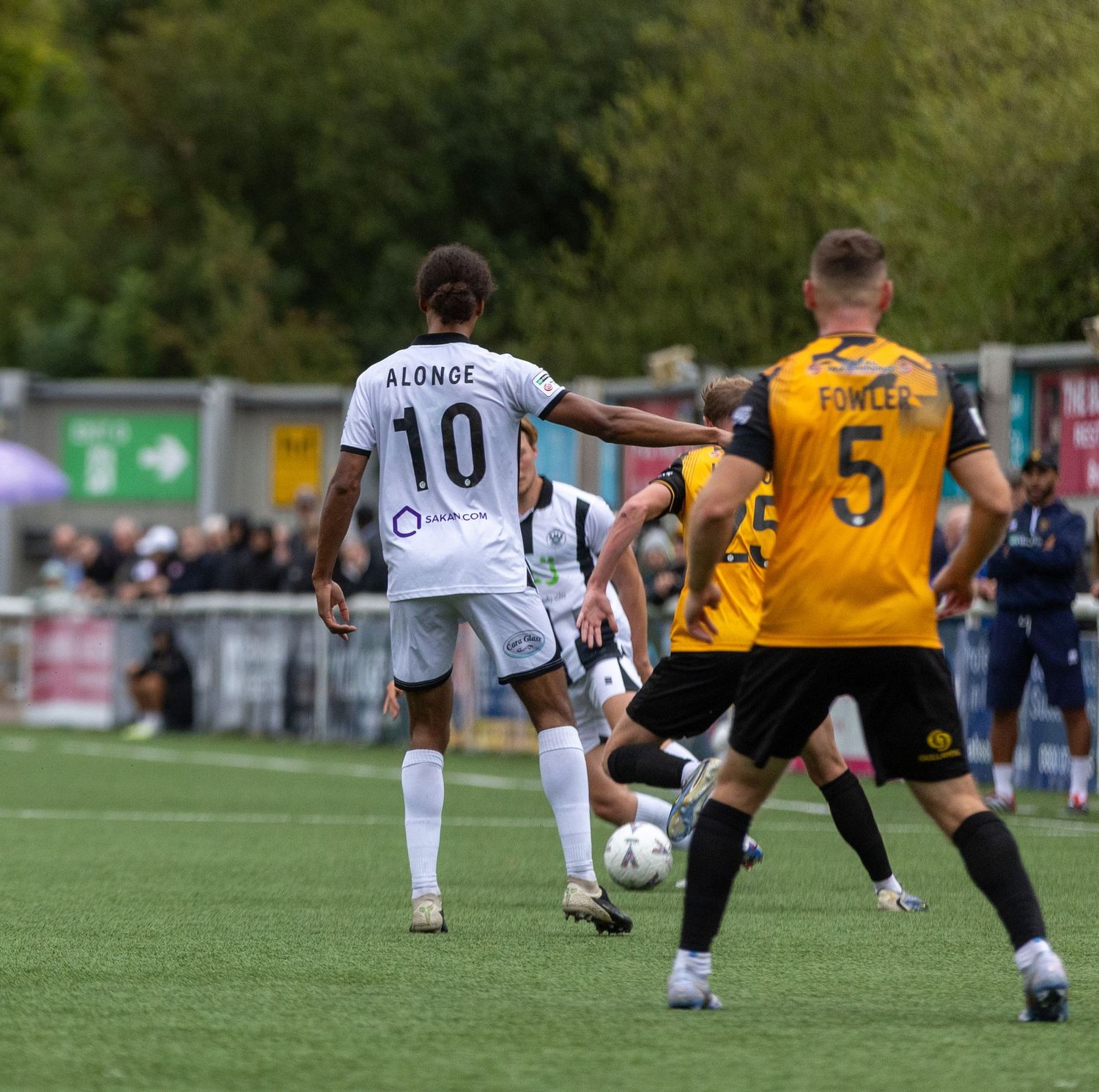 Soccer players in action, number 10 Alonge in white kit competing against number 5 in yellow during an outdoor match.