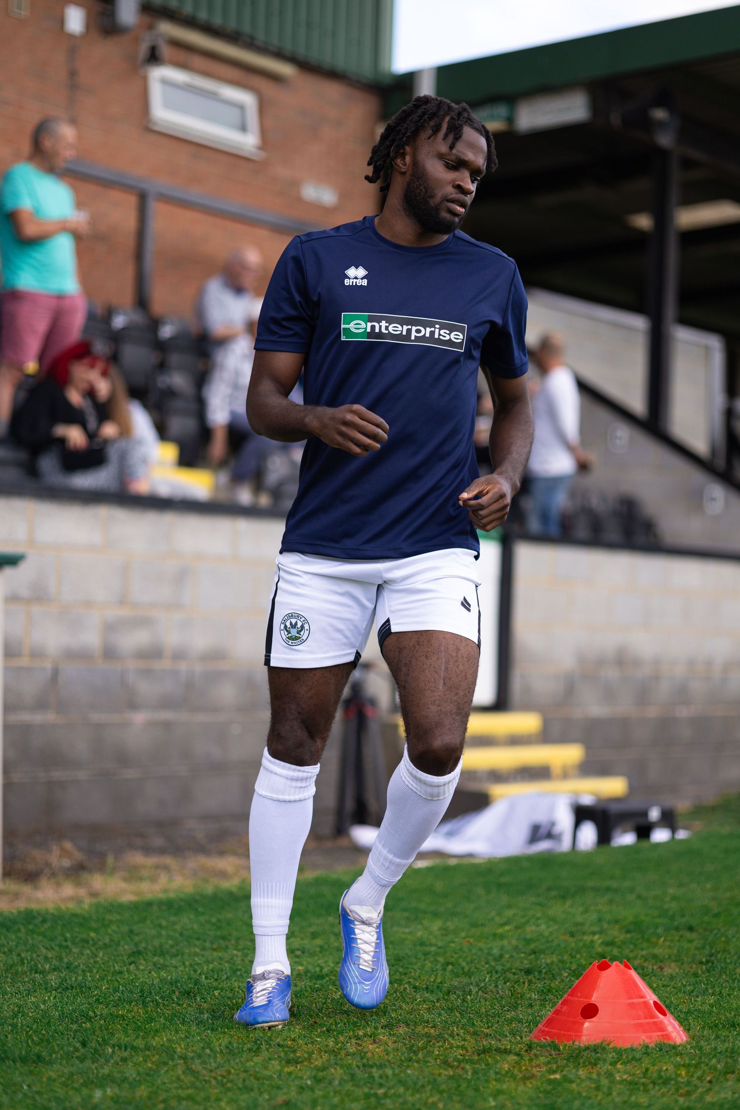 Football player in navy Enterprise-sponsored kit warming up on grass pitch during pre-match training session.
