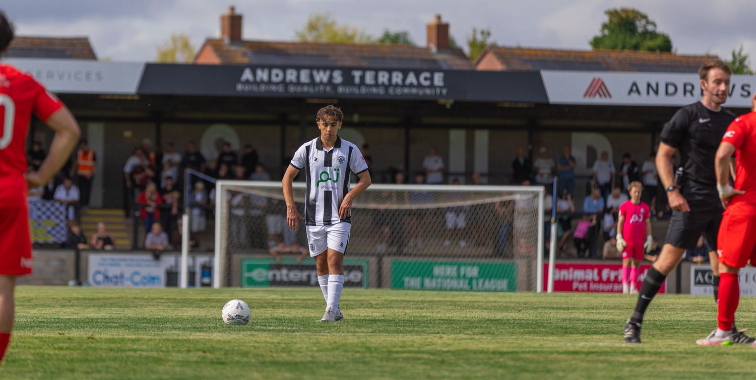 Soccer player in black and white kit prepares to take a free kick outside Andrews Terrace stadium.