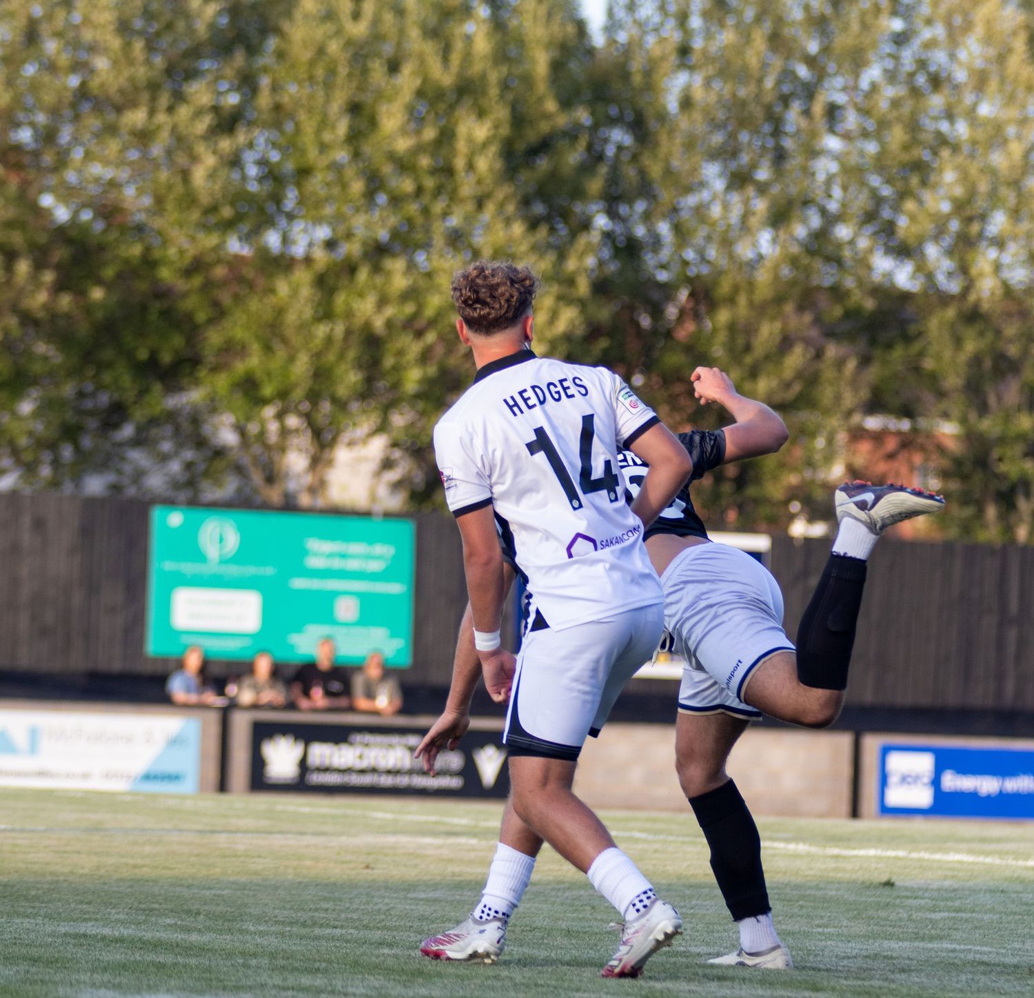 Two football players compete for ball, player number 14 Hedges in white kit mid-action.