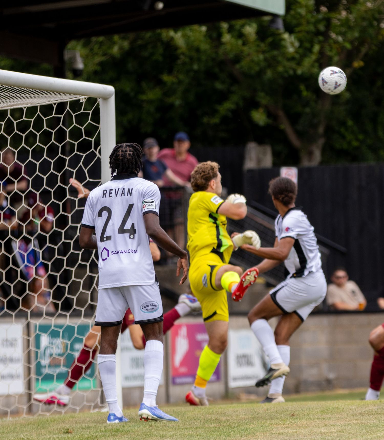 A goalkeeper in yellow kit catches the ball as number 24 Revan watches during a match.