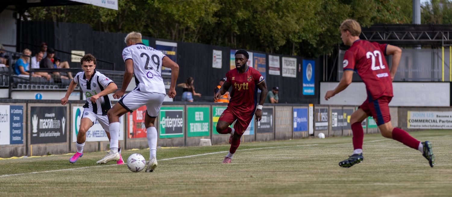 Soccer players number 29 and 22 compete during match on green pitch with spectators in background.