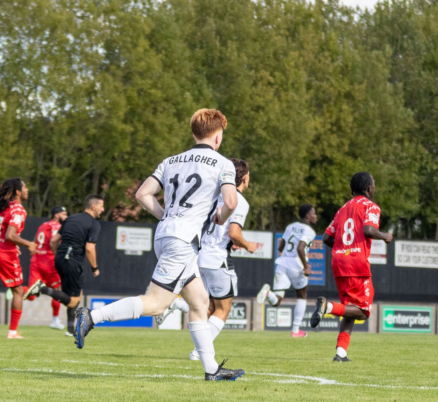 Player number 12 Gallagher runs during a football match in black and white kit against red team.