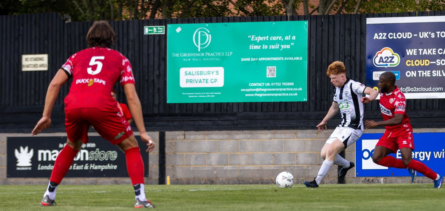 A black-and-white kitted player prepares to shoot as red-kitted number 5 closes in near advertising hoardings.