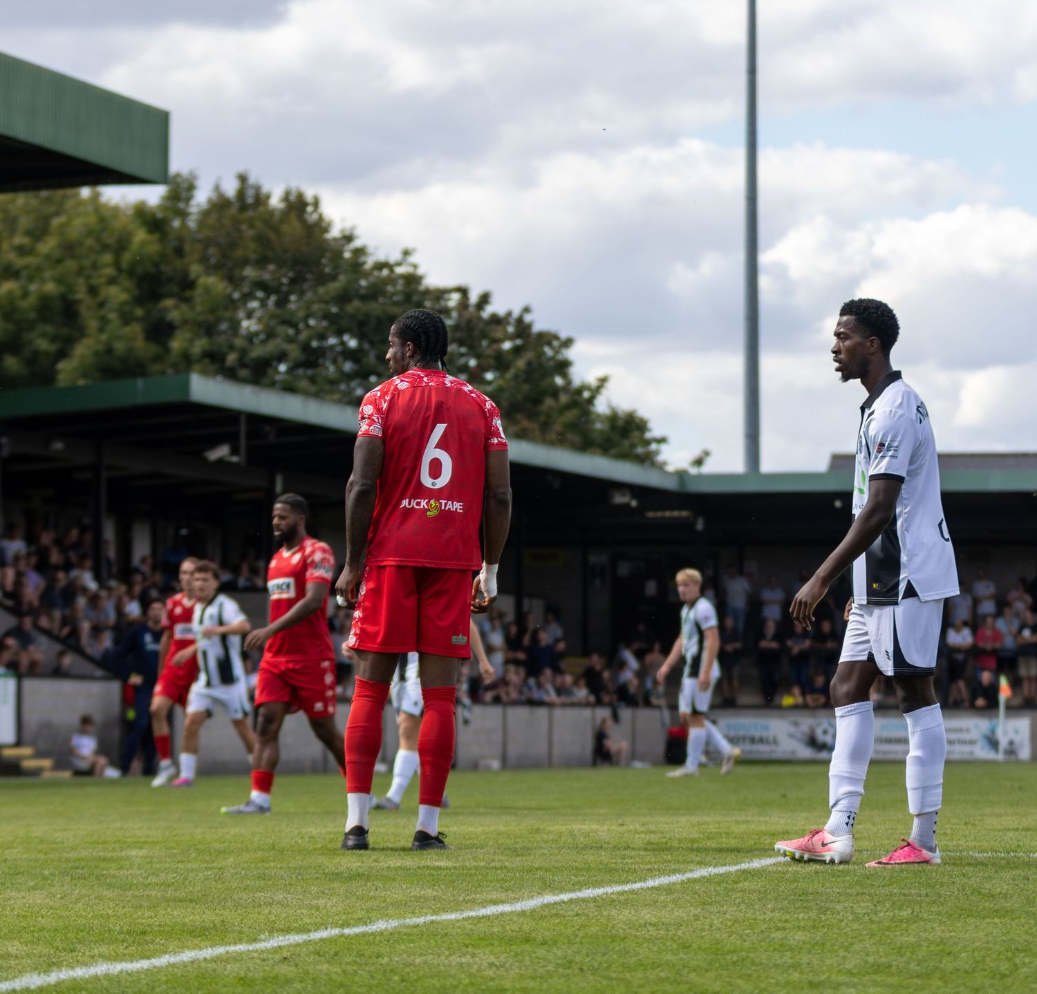 Football players in red and white kits stand on the pitch during a match pause.