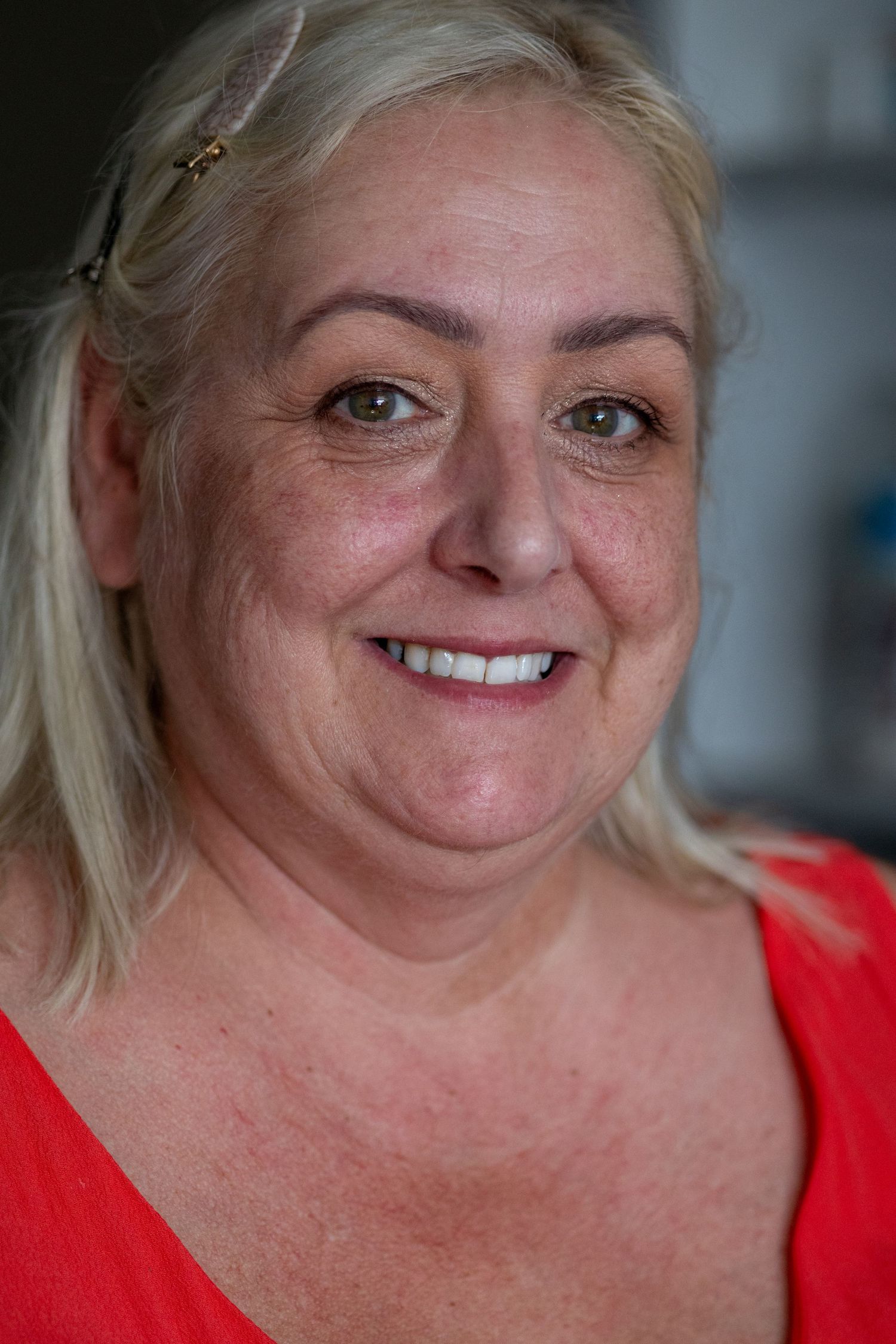 Smiling mature blonde woman in red top with natural makeup and warm expression.