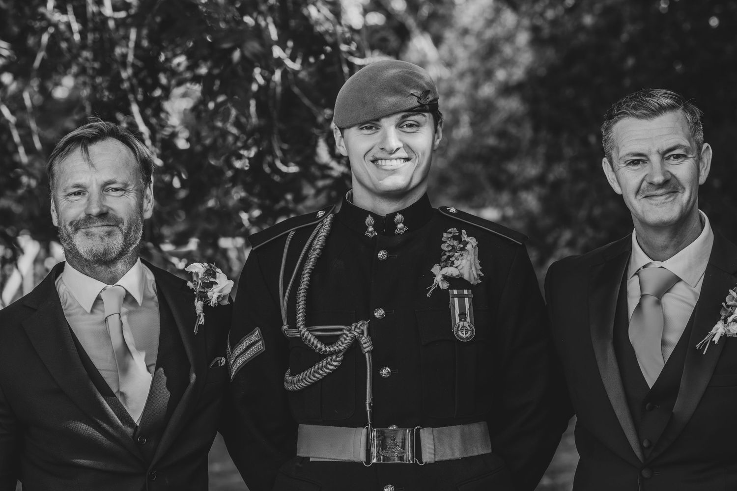Black and white photo of three men at a wedding, center man wearing military dress uniform.