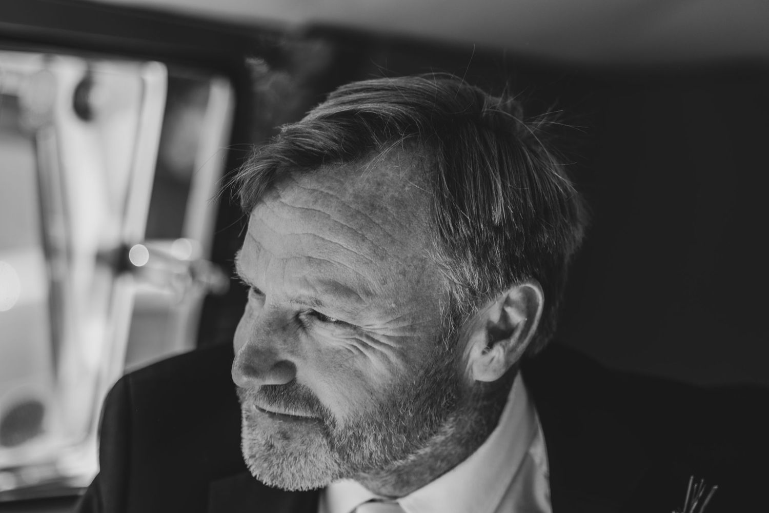 Black and white portrait of a distinguished older gentleman in a suit at a wedding celebration.