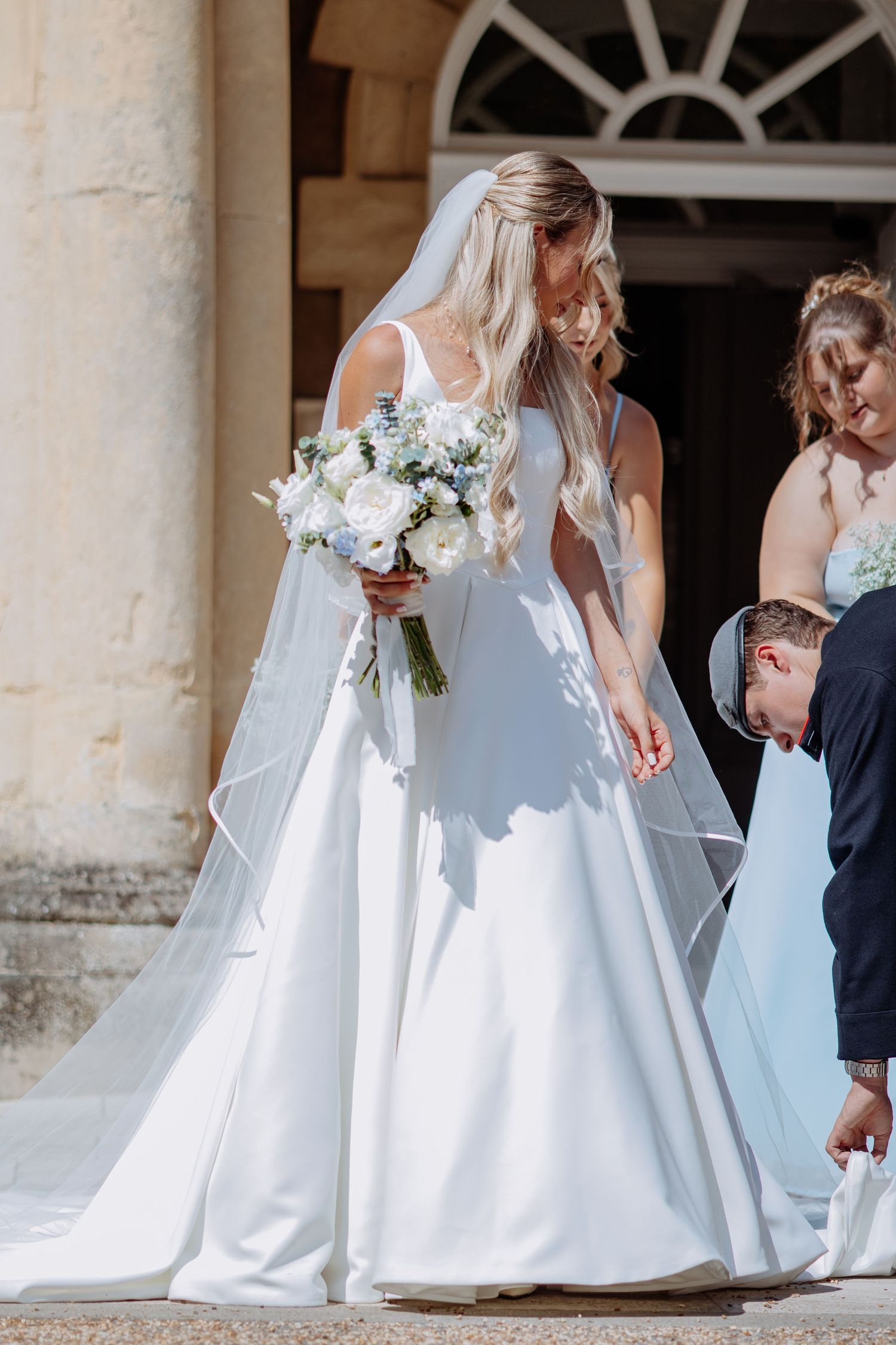 Elegant bride in white ball gown holds white bouquet outside wedding venue.