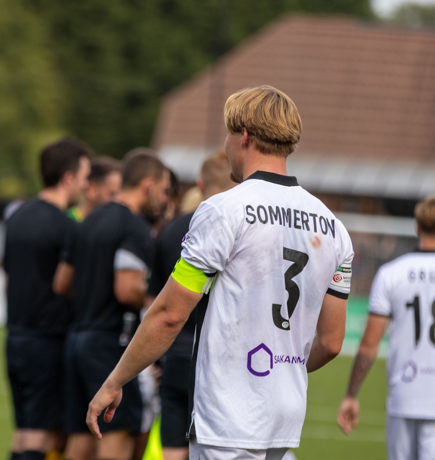Soccer player Sommerton wearing number 3 white jersey with captain armband stands on the pitch.