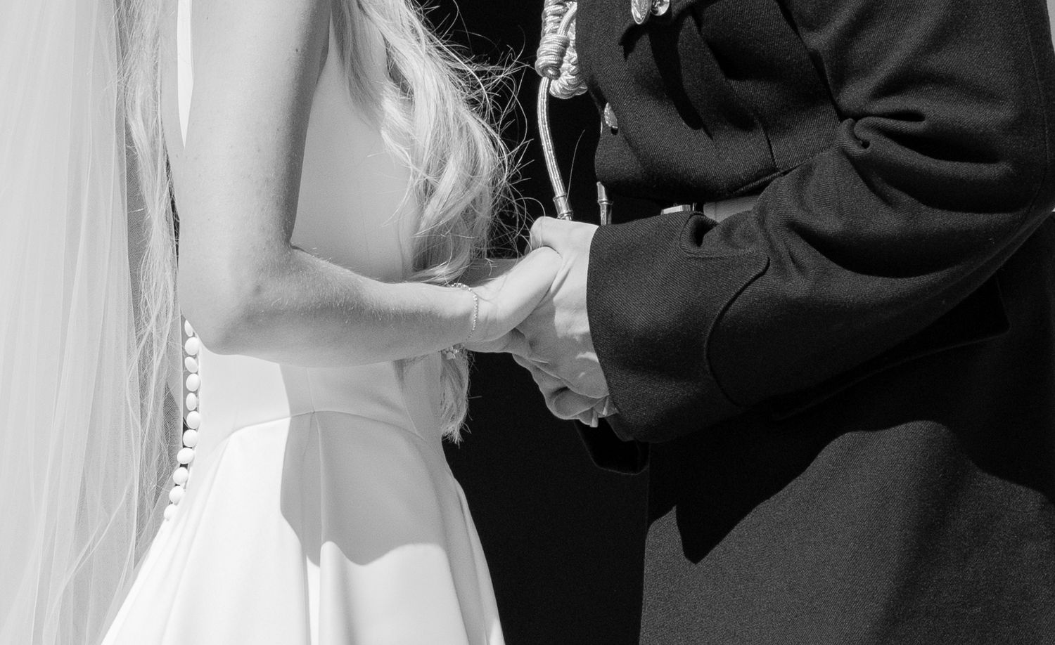 Black and white close-up of bride and groom holding hands during their wedding ceremony.