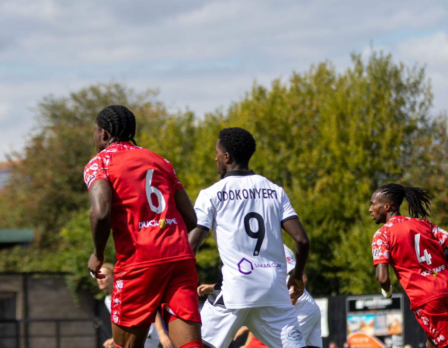 Three footballers compete for aerial ball with player number 9 in white between two red opponents.
