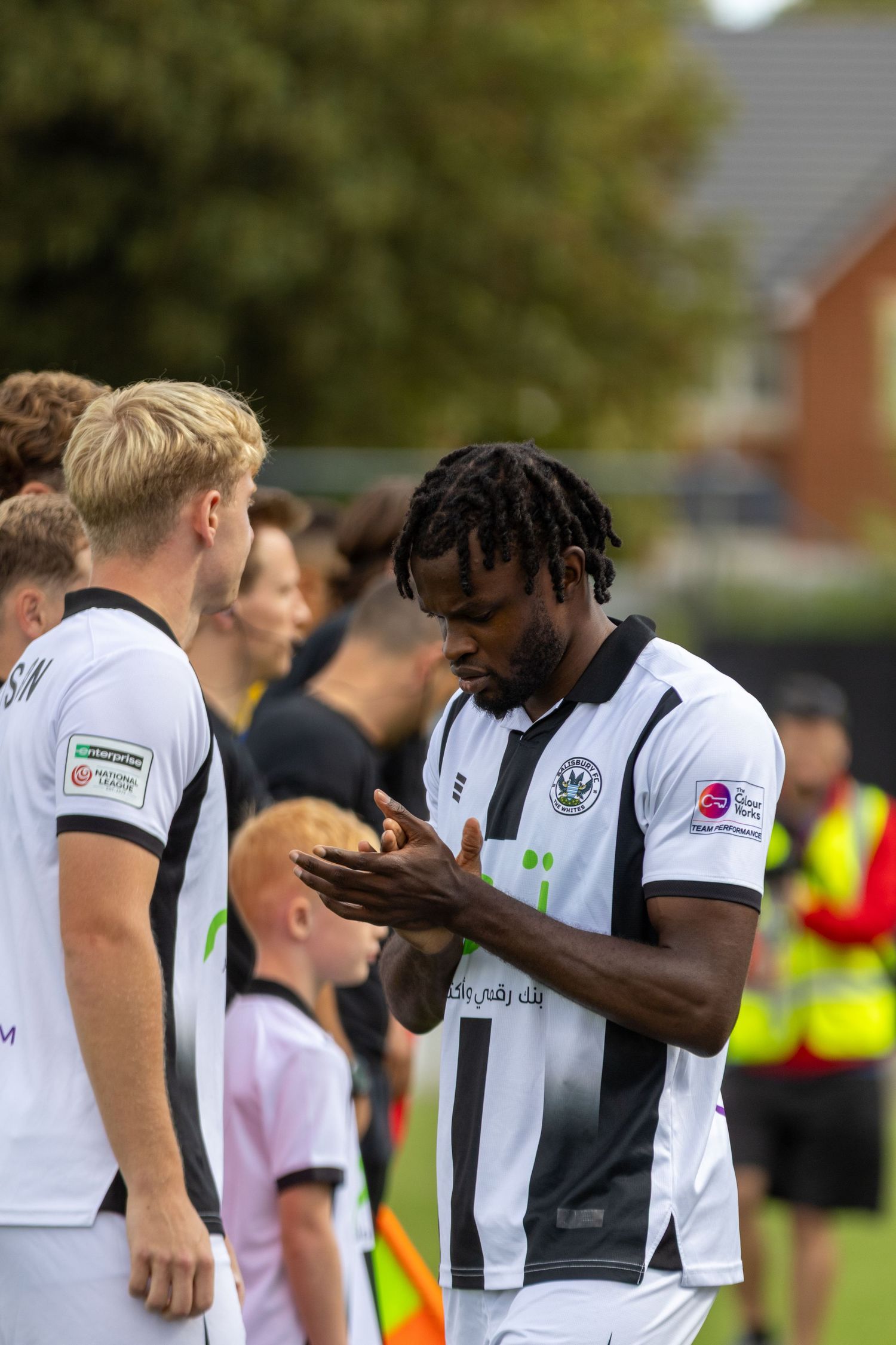 A footballer in a black and white striped kit looks at his hands before a match.