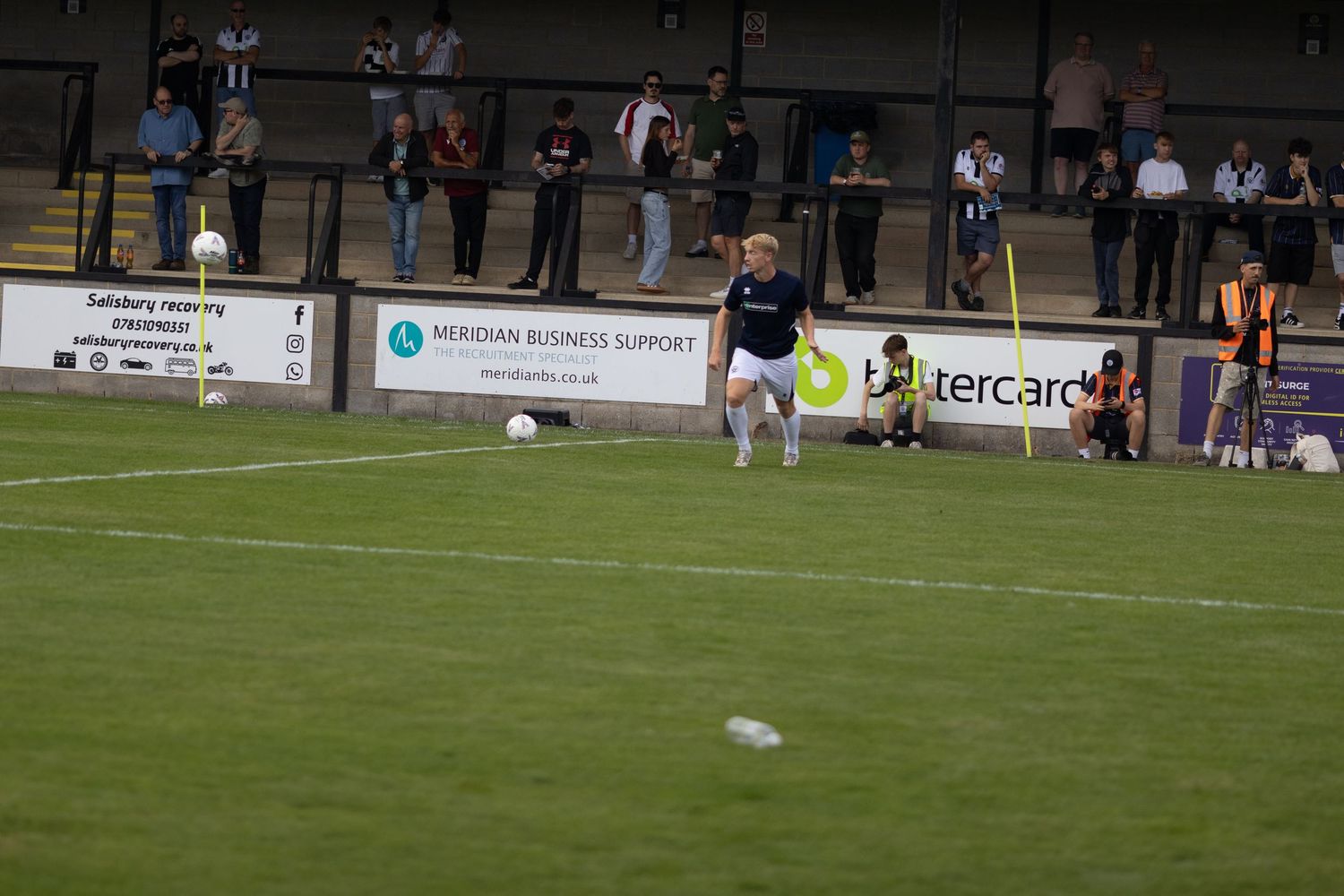 A footballer in navy blue kit dribbles the ball along the pitch during a competitive football match.