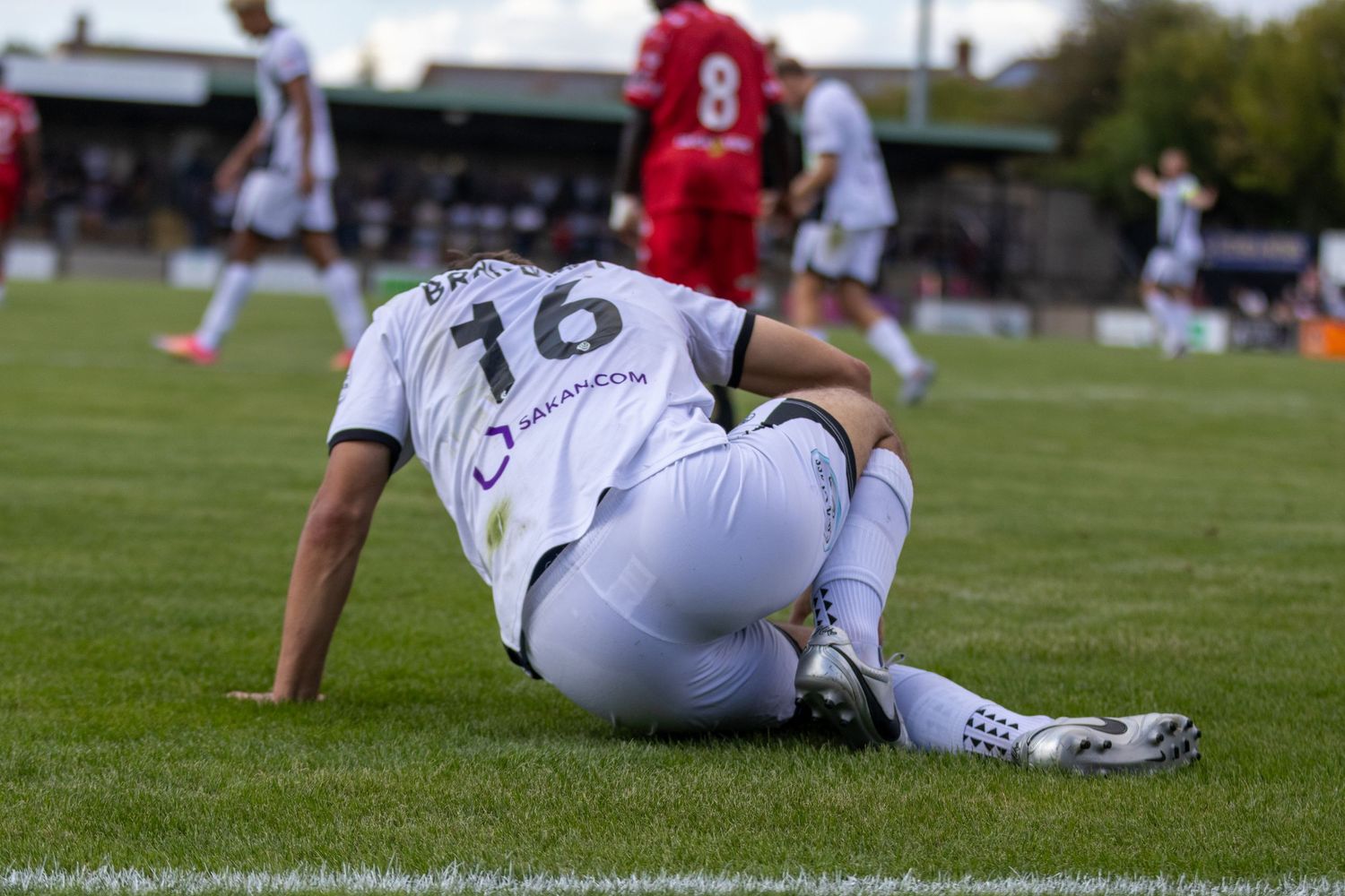Soccer player number 16 sits on the ground injured during a competitive match.