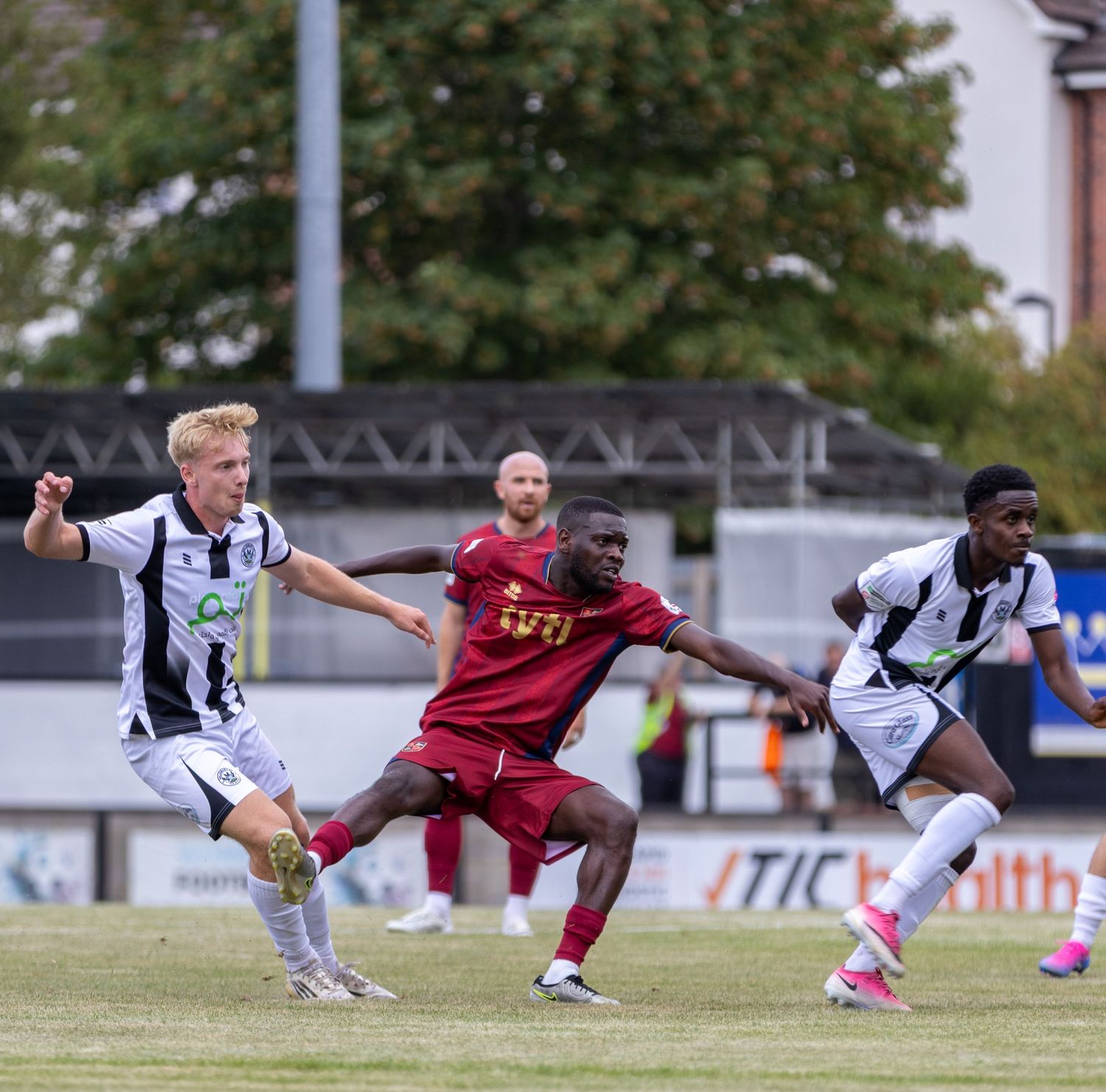 White-kitted player challenges maroon opponent for ball during competitive outdoor football match.