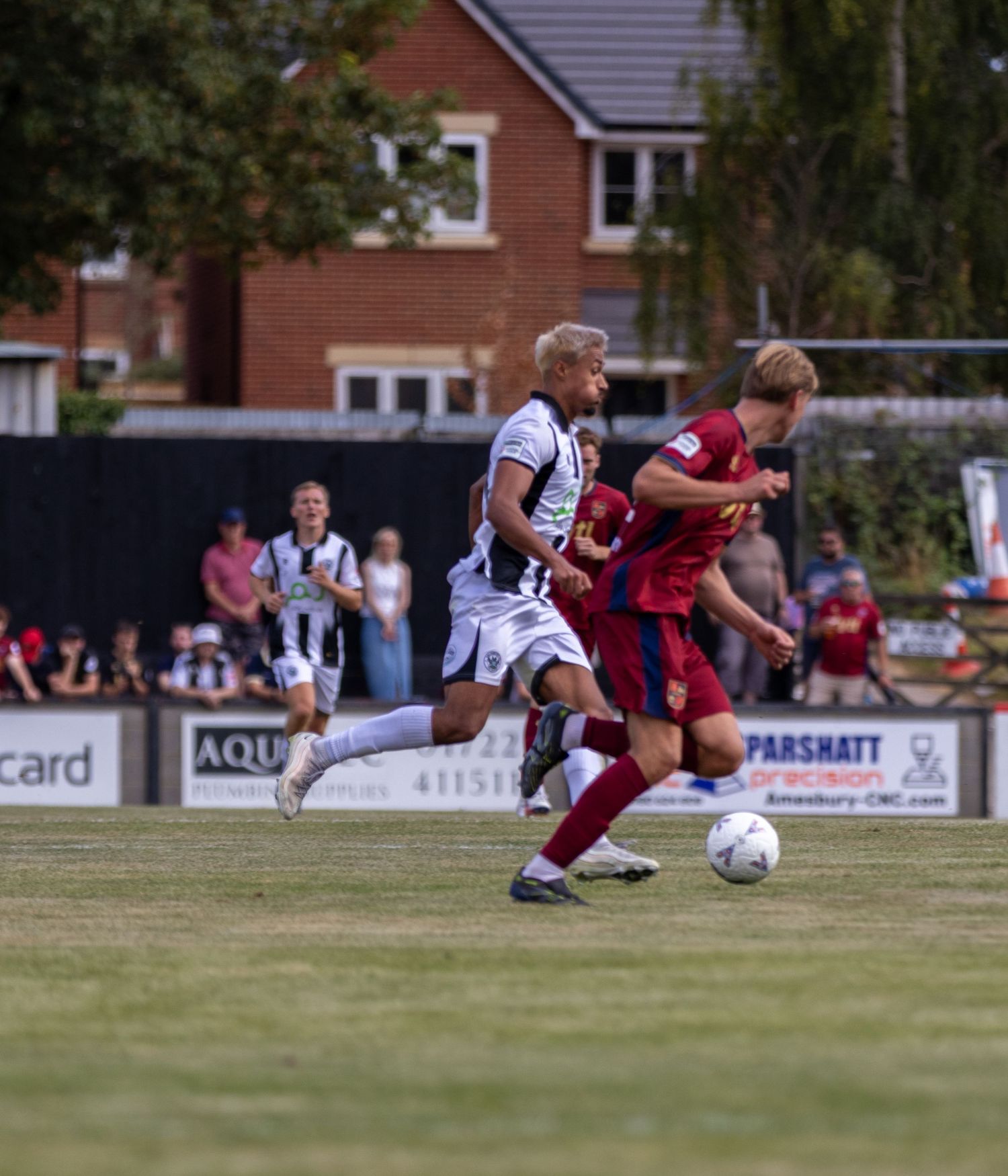 Two football players compete for the ball along the sideline during a sunny outdoor football match.