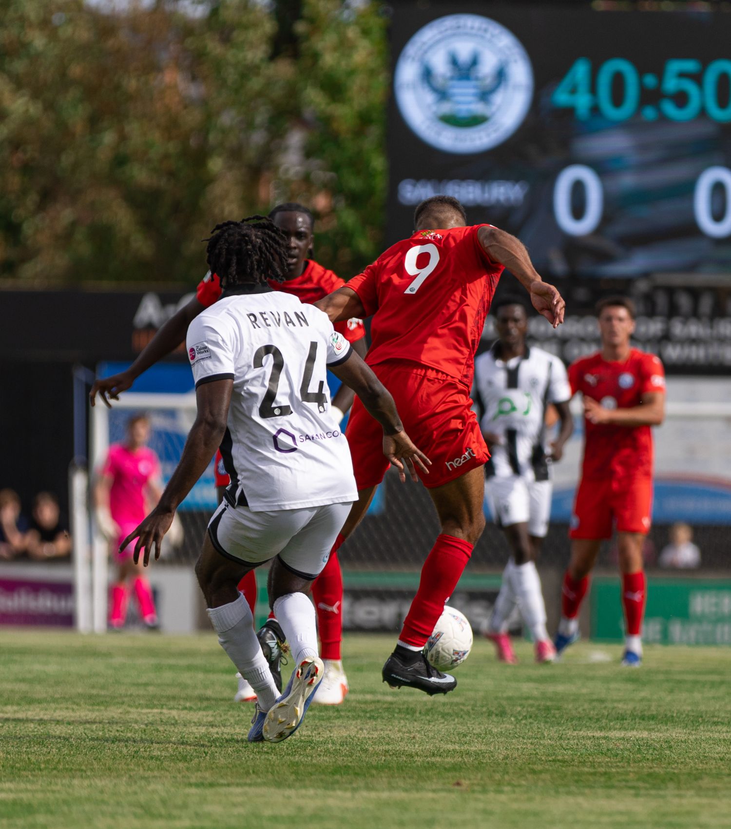 Soccer players compete for the ball during a match, with player number 9 in red challenging player number 24 in white.