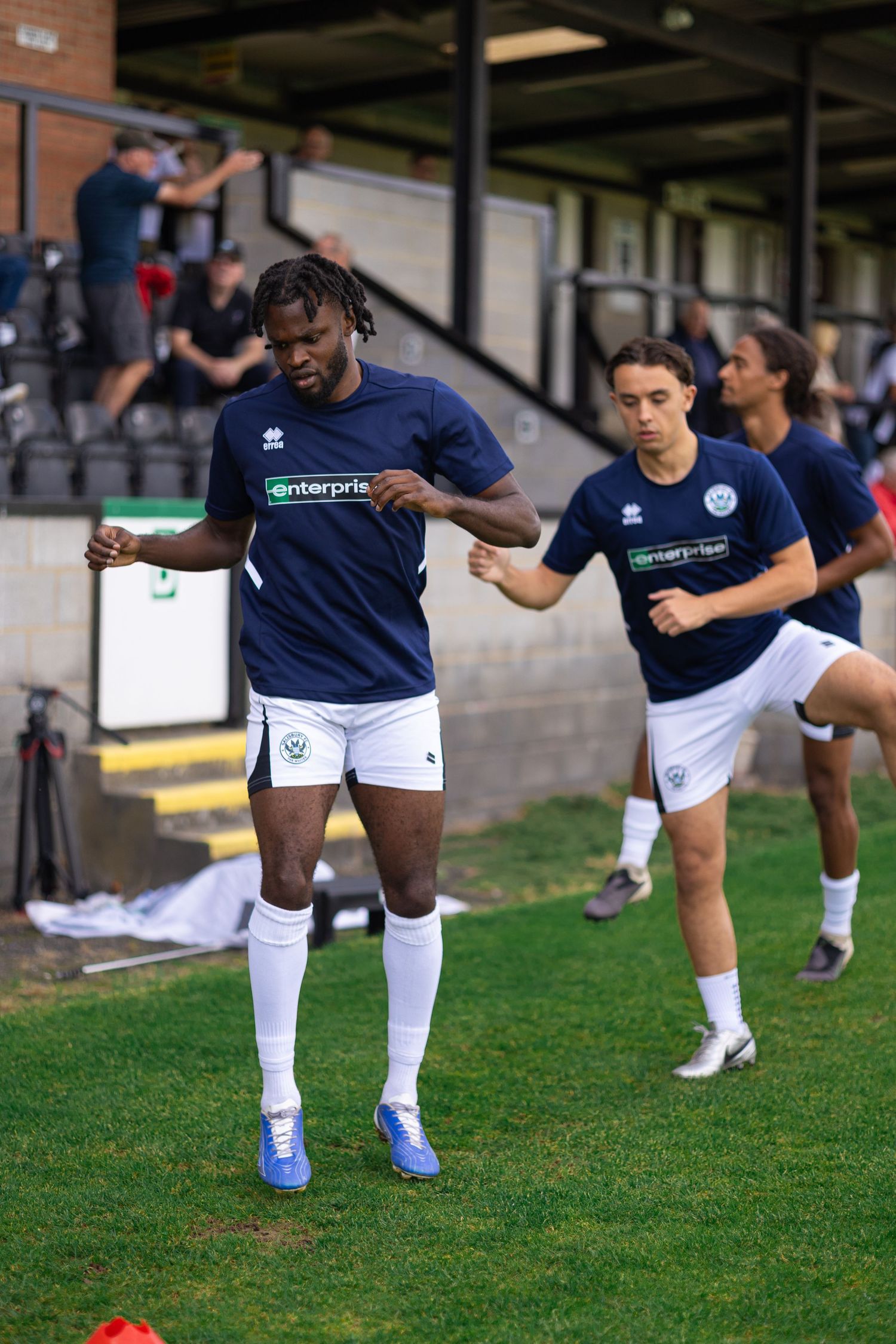 Football players in navy Enterprise-sponsored kits warming up on grass pitch before a match at a stadium.