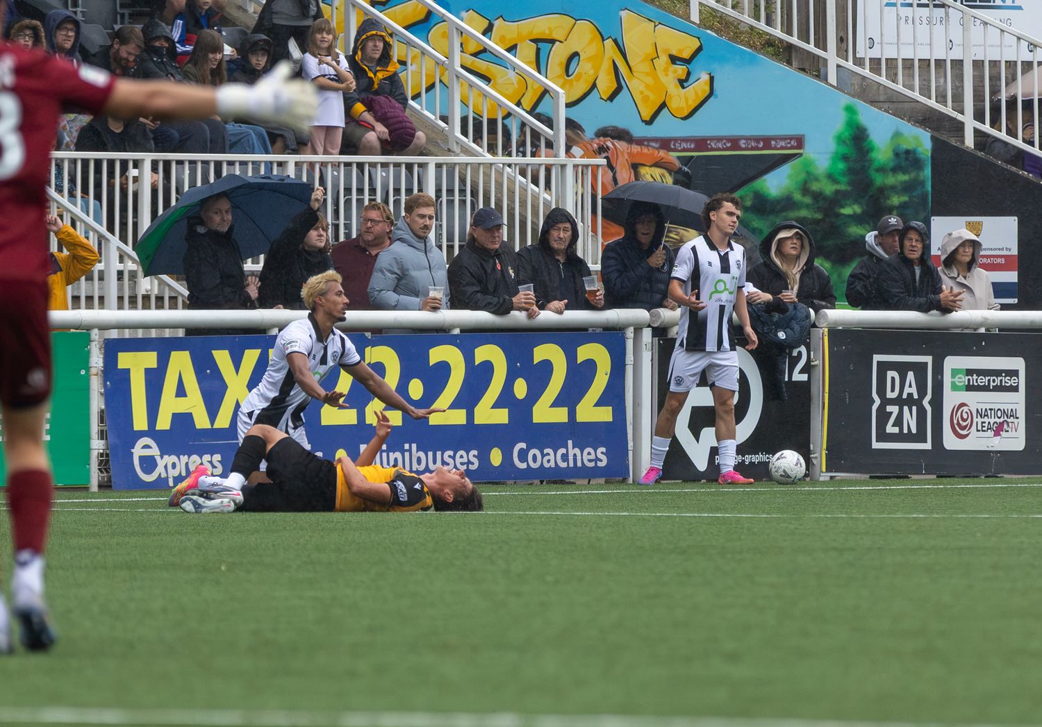Football players in black and white striped kits compete on a wet pitch during a rainy match day.