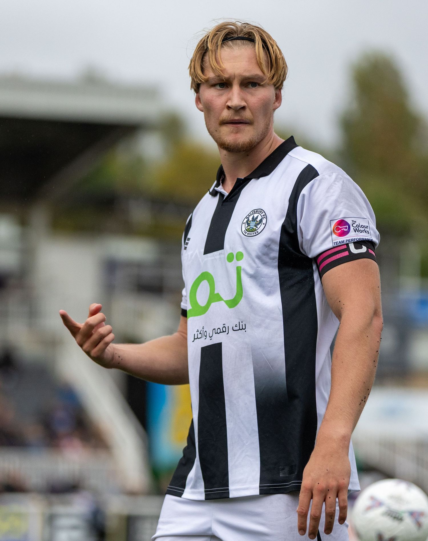 Male footballer in black and white striped jersey with sponsor logo, standing on pitch during a match.