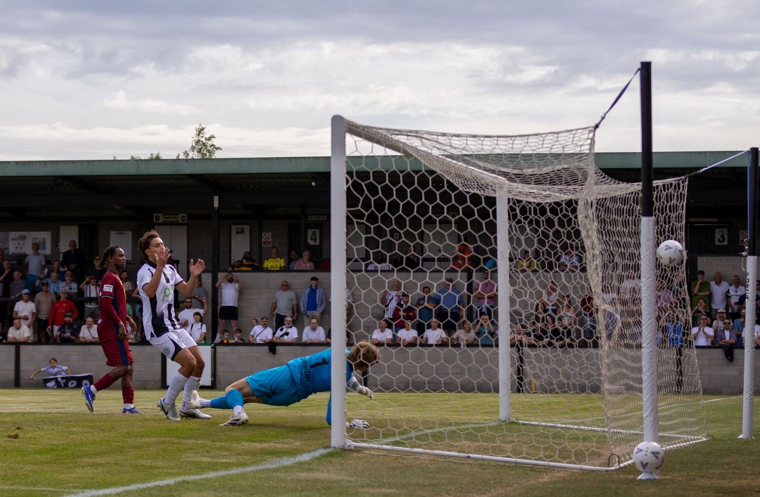 Goalkeeper dives to the ground as a football rolls toward the net during a competitive match.