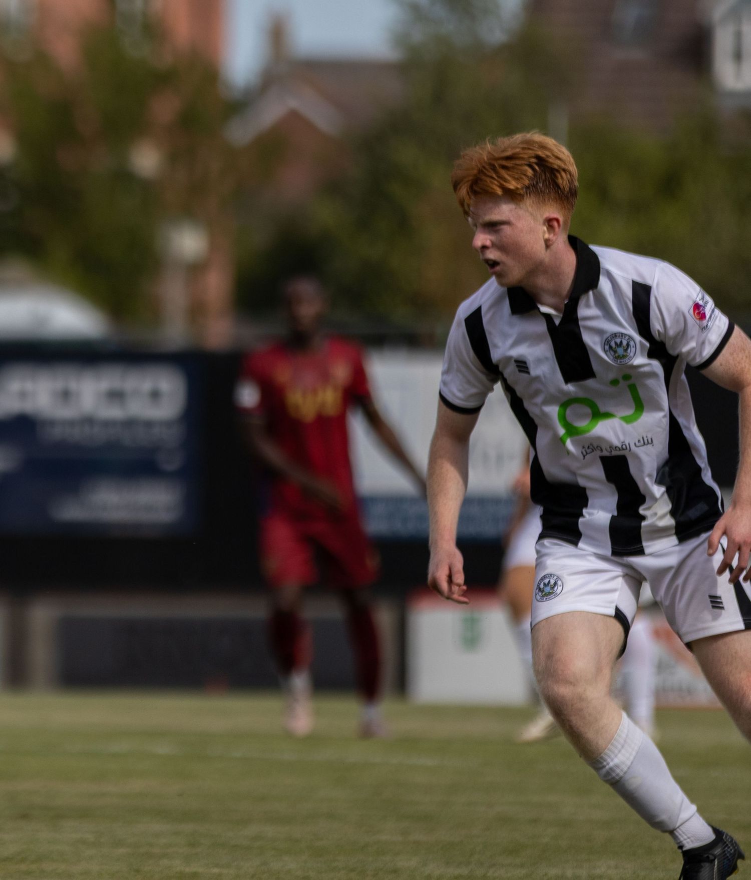 Young red-haired footballer in black and white strip runs during a sunny outdoor football match.