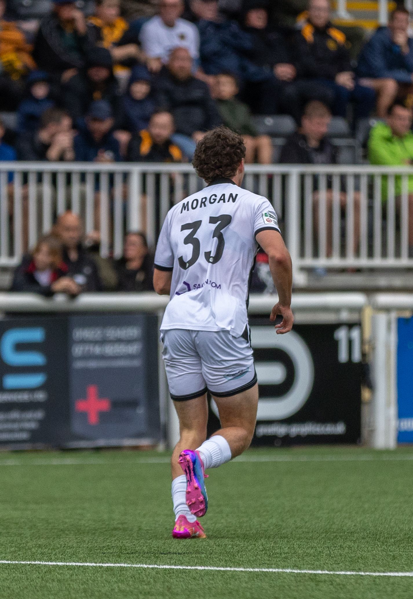 Soccer player Morgan, number 33, walks on the field in a white away kit with pink cleats.
