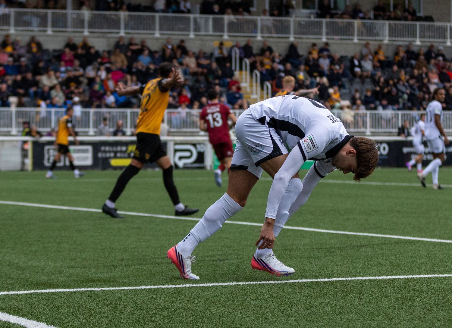 Soccer player in white uniform bending over on field during a competitive match at a stadium.