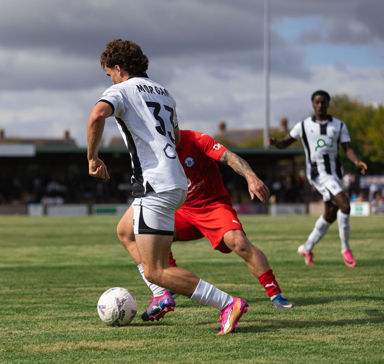 Two soccer players compete for the ball during a sunny outdoor match, one wearing number 33 in white, the other in red.