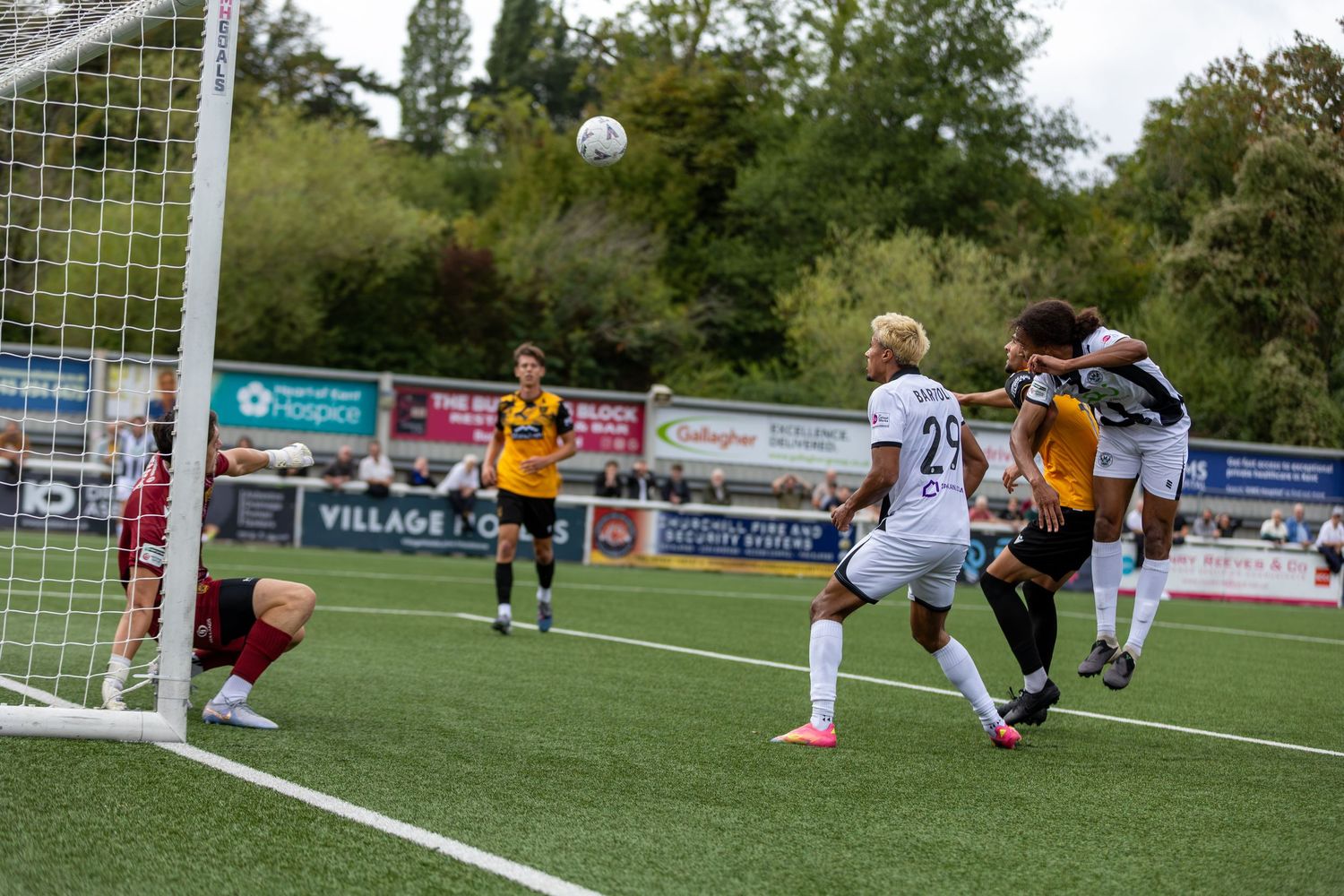 Soccer players compete for a header near the goal during an outdoor match at a local football ground.