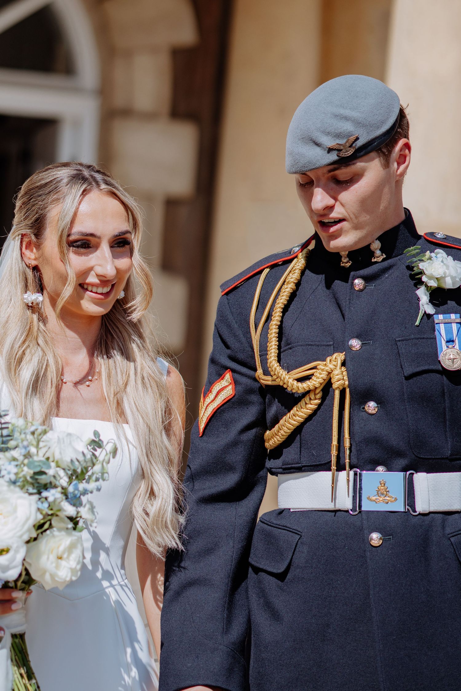 Bride in white gown smiles beside groom wearing RAF blue dress uniform with gold lanyard and medals.