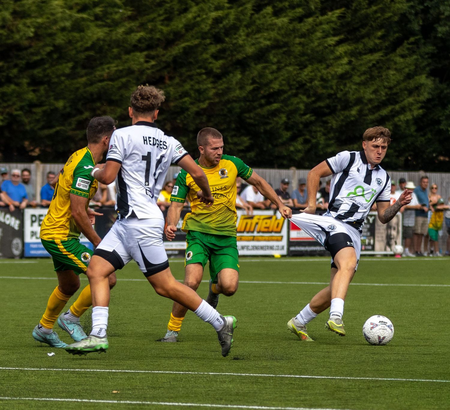 Players in yellow-green and white kits battle for possession during an intense football match.