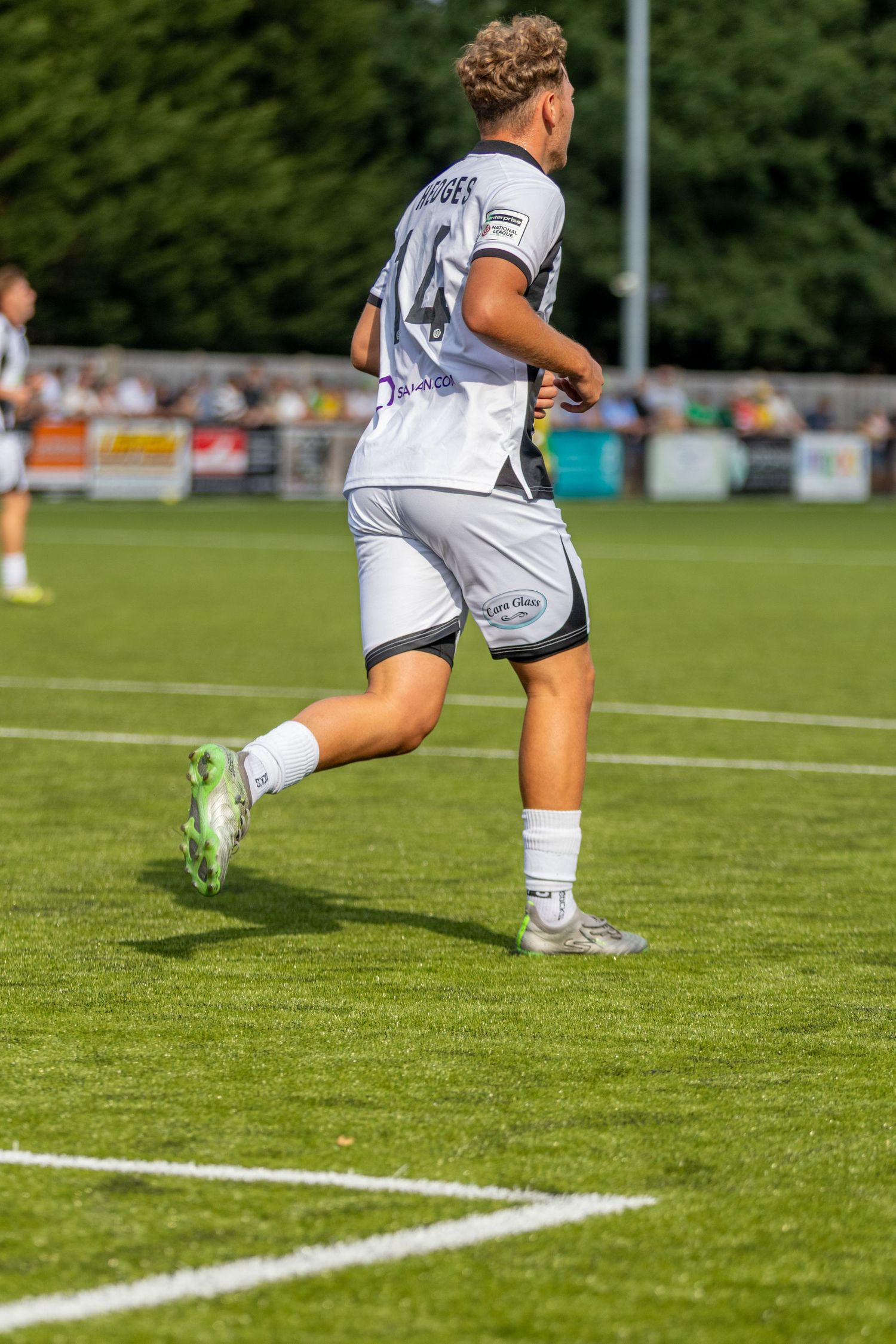 A footballer wearing number 46 in white away kit runs along the touchline during a sunny football match.