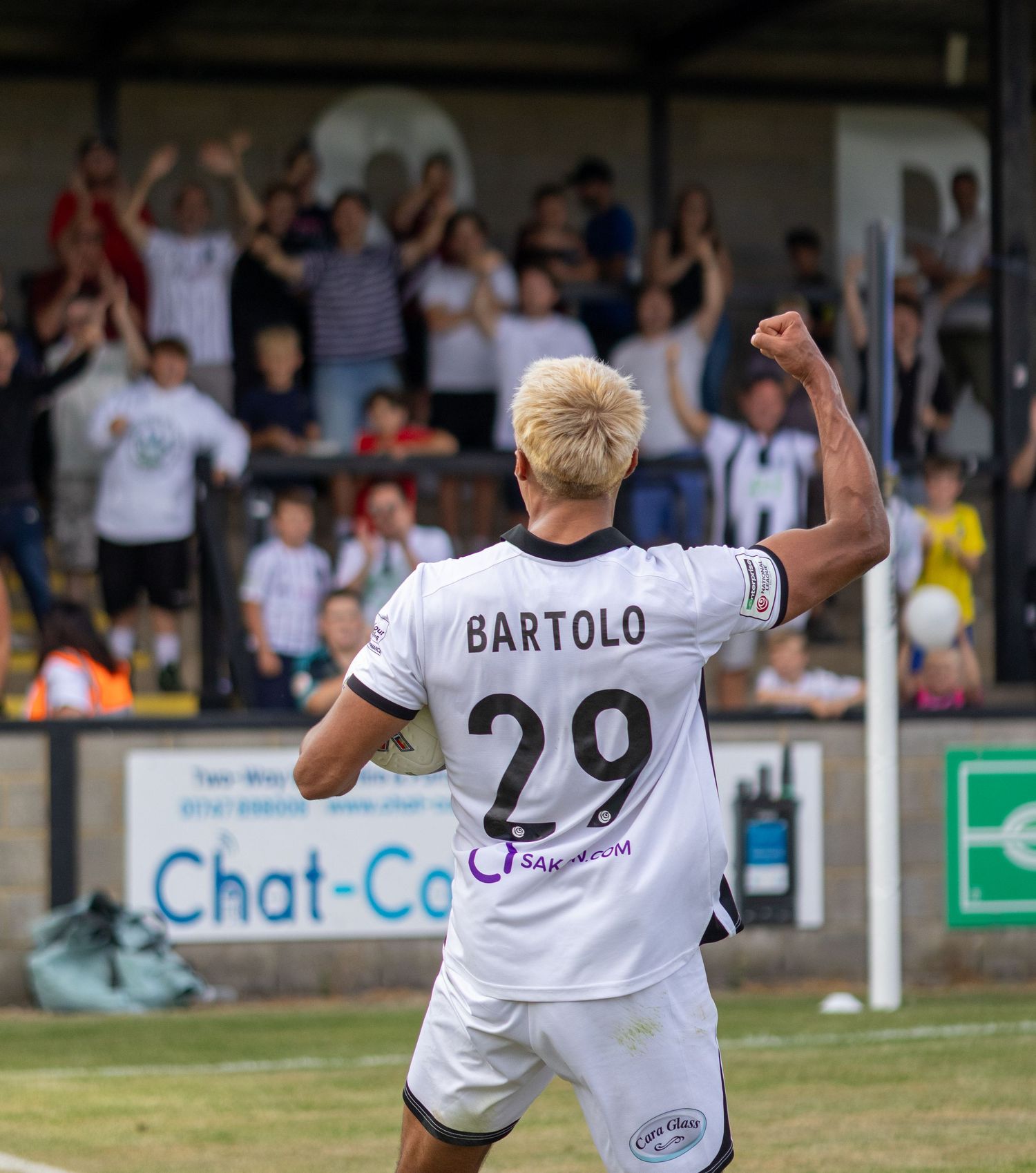 Soccer player Bartolo number 29 pumps fist in triumph as excited fans celebrate behind him.