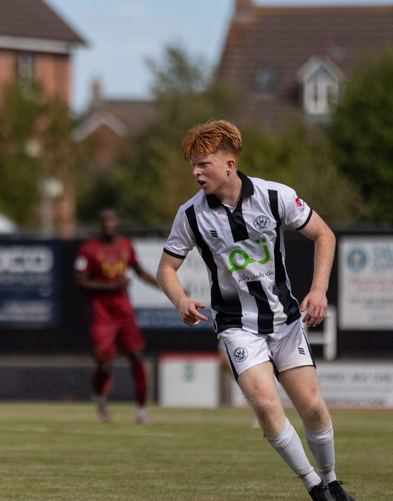 Young red-haired footballer in black and white kit dribbles during a sunny outdoor football match.