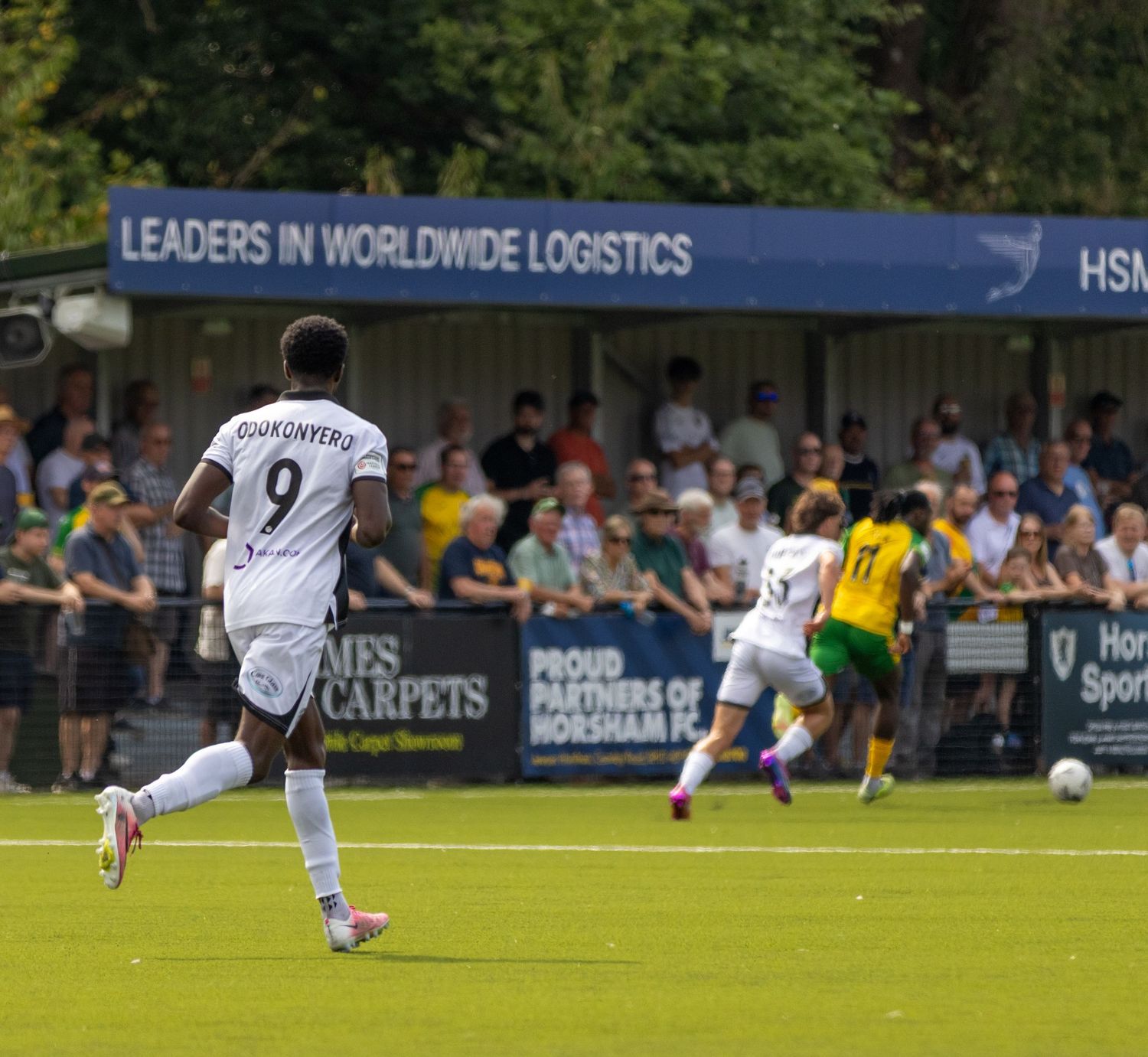 Footballer wearing number 9 runs toward goal during an outdoor match with a banner reading Leaders in Worldwide Logistics.