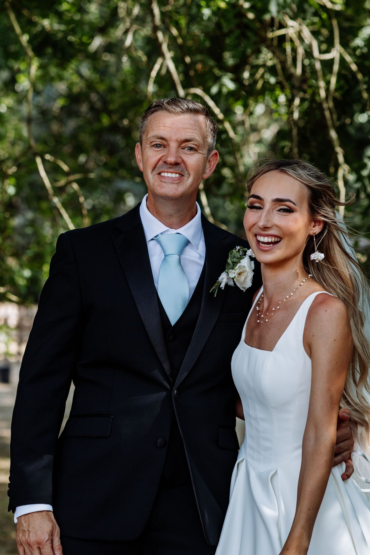 Smiling groom in black tuxedo with mint tie and bride in white wedding dress posing outdoors.