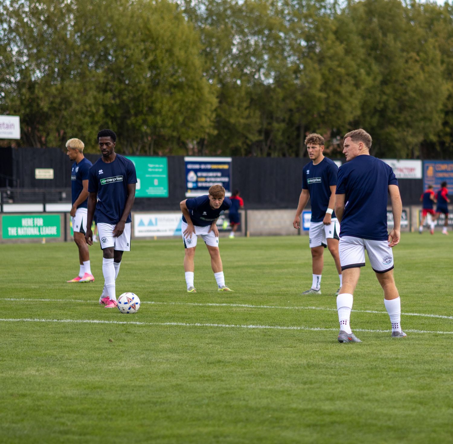 Group of football players in navy uniforms stretching and warming up on a grass pitch before a game.