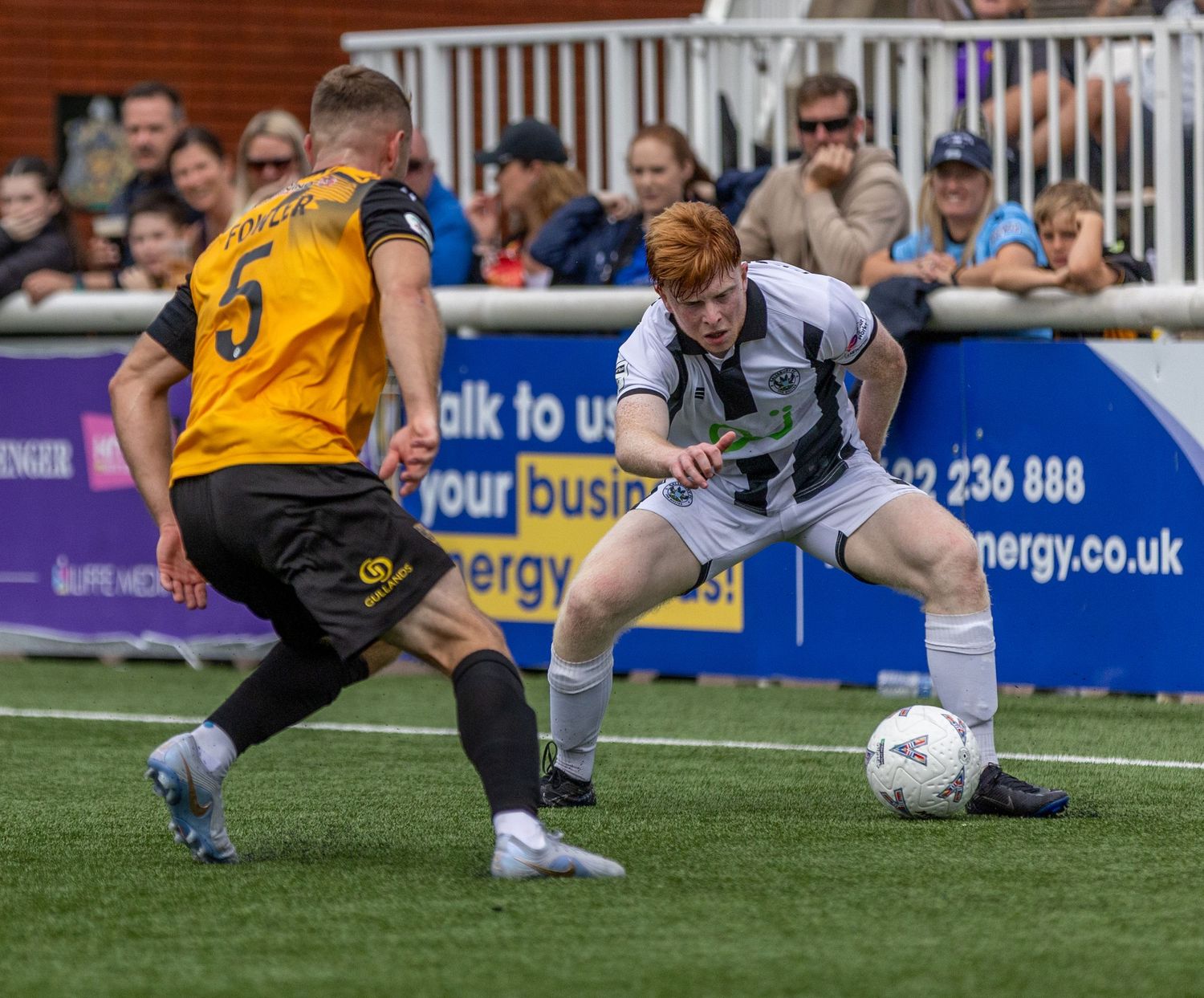 Two soccer players compete for the ball during a match, one in black and white kit, the other in yellow and black.