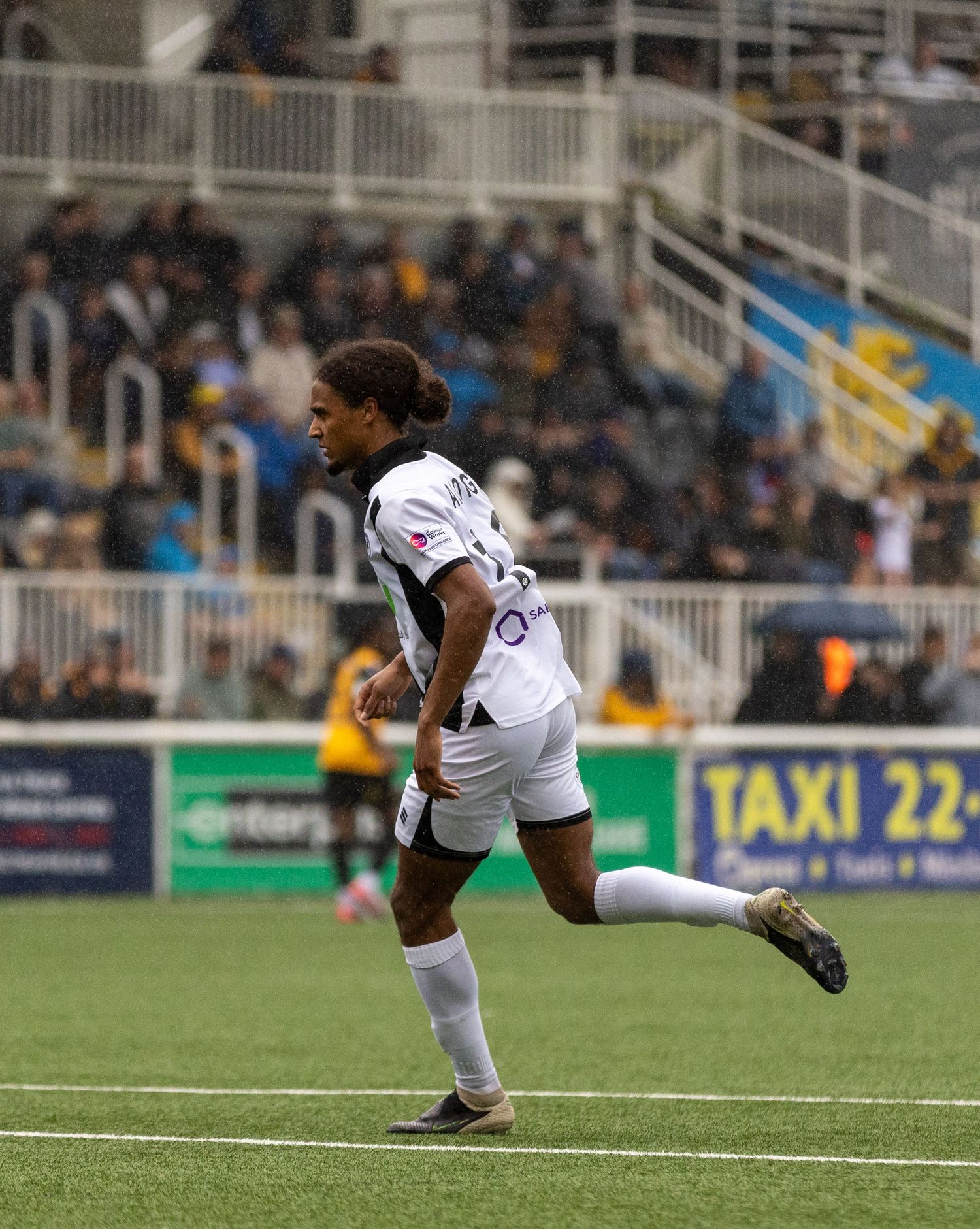 Soccer player in white uniform running on green turf field during a match at a stadium.