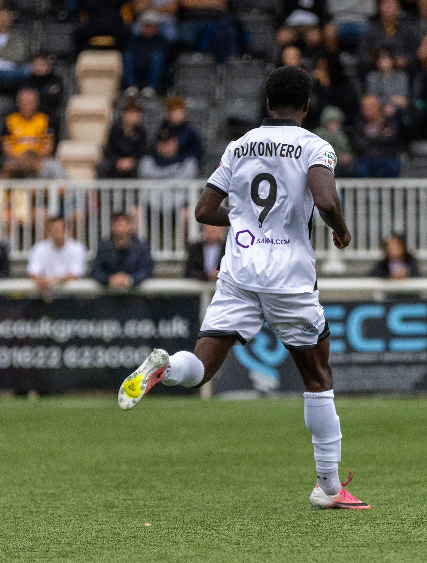 Soccer player Dukonyero wearing number 9 white jersey dribbles ball during a match at a stadium.
