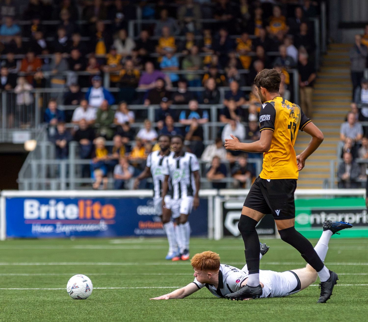 Two soccer players in action, one sliding on the ground near the ball during a match at a stadium.