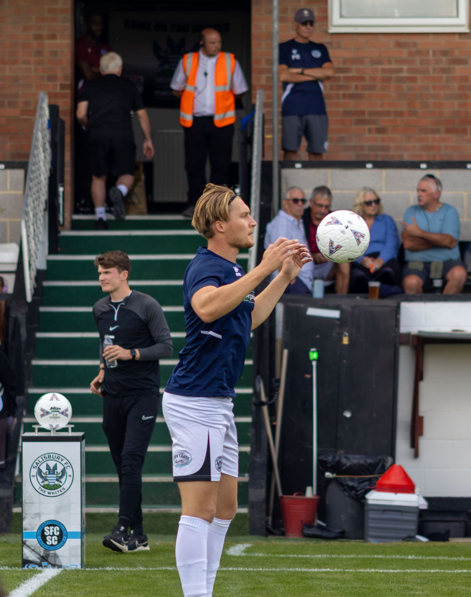 A footballer in navy blue kit prepares to take a throw-in during a football match at a stadium.