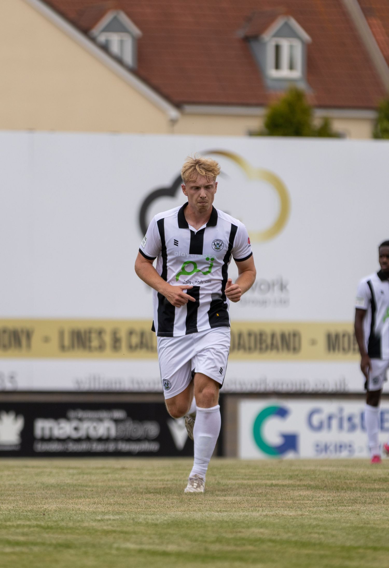 Young blonde footballer in black and white striped jersey runs during outdoor daytime match.