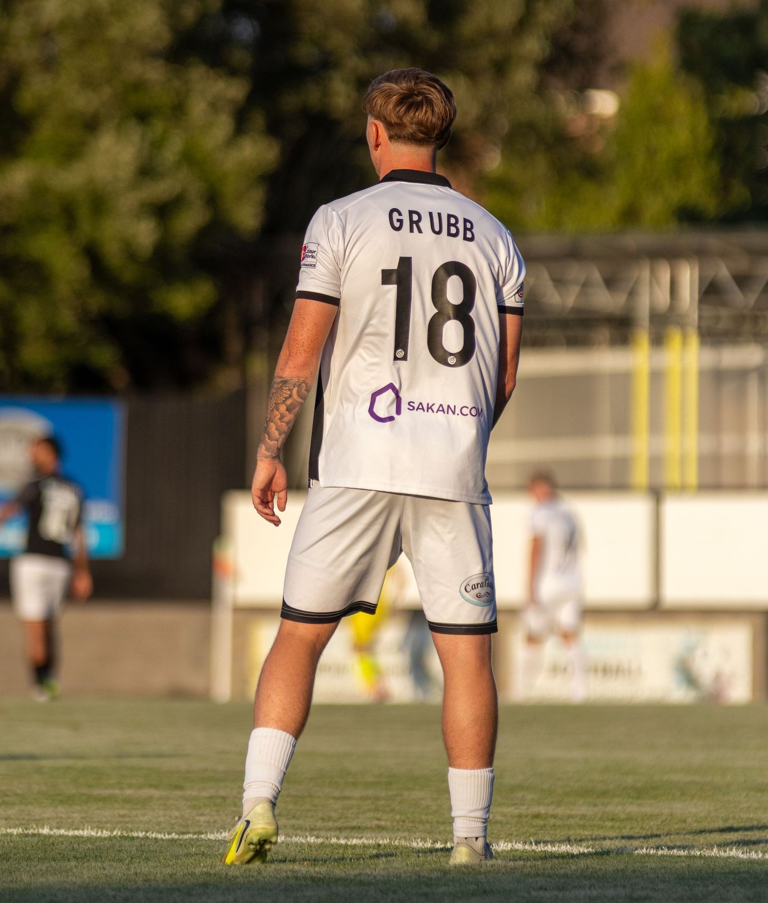 Rear view of footballer Grubb wearing number 18 white kit with Sakan.com sponsor on the pitch.