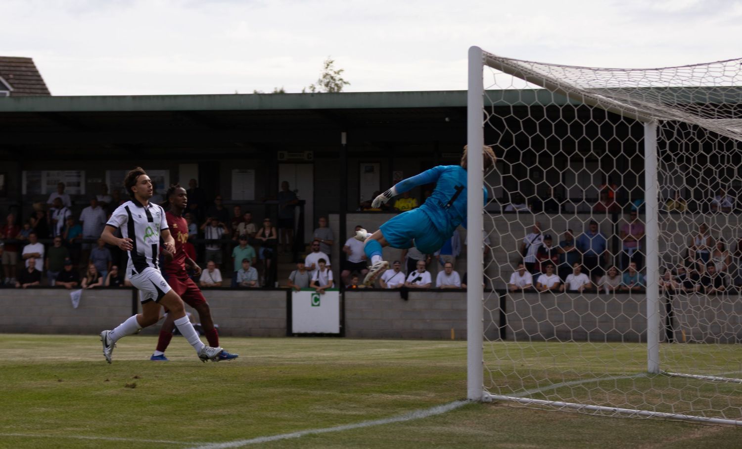 Goalkeeper dives through the air attempting to save a shot on goal during a football match.