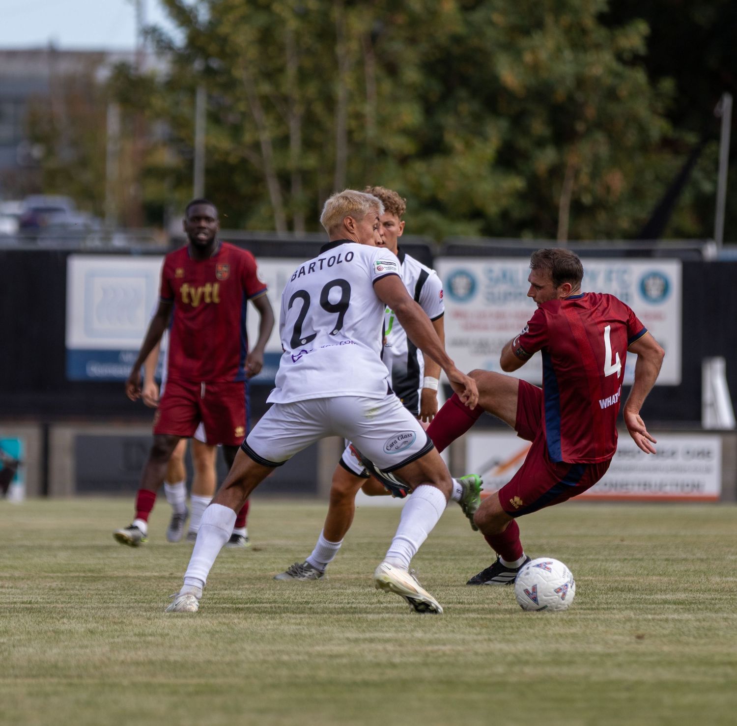 Player number 29 BARTOLO dribbles ball past sliding tackle during competitive outdoor soccer match.
